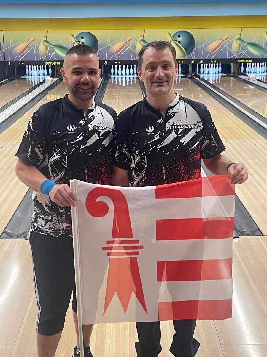 Deux joueurs du Team Jura en polo du club, avec le drapeau jurassien, devant les pistes de bowling